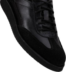 A pair of black suede leather semi-formal trainers with a lace-up closure and a thick sole.