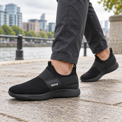 QUIVE black slip-on walking trainers worn on a British riverside promenade