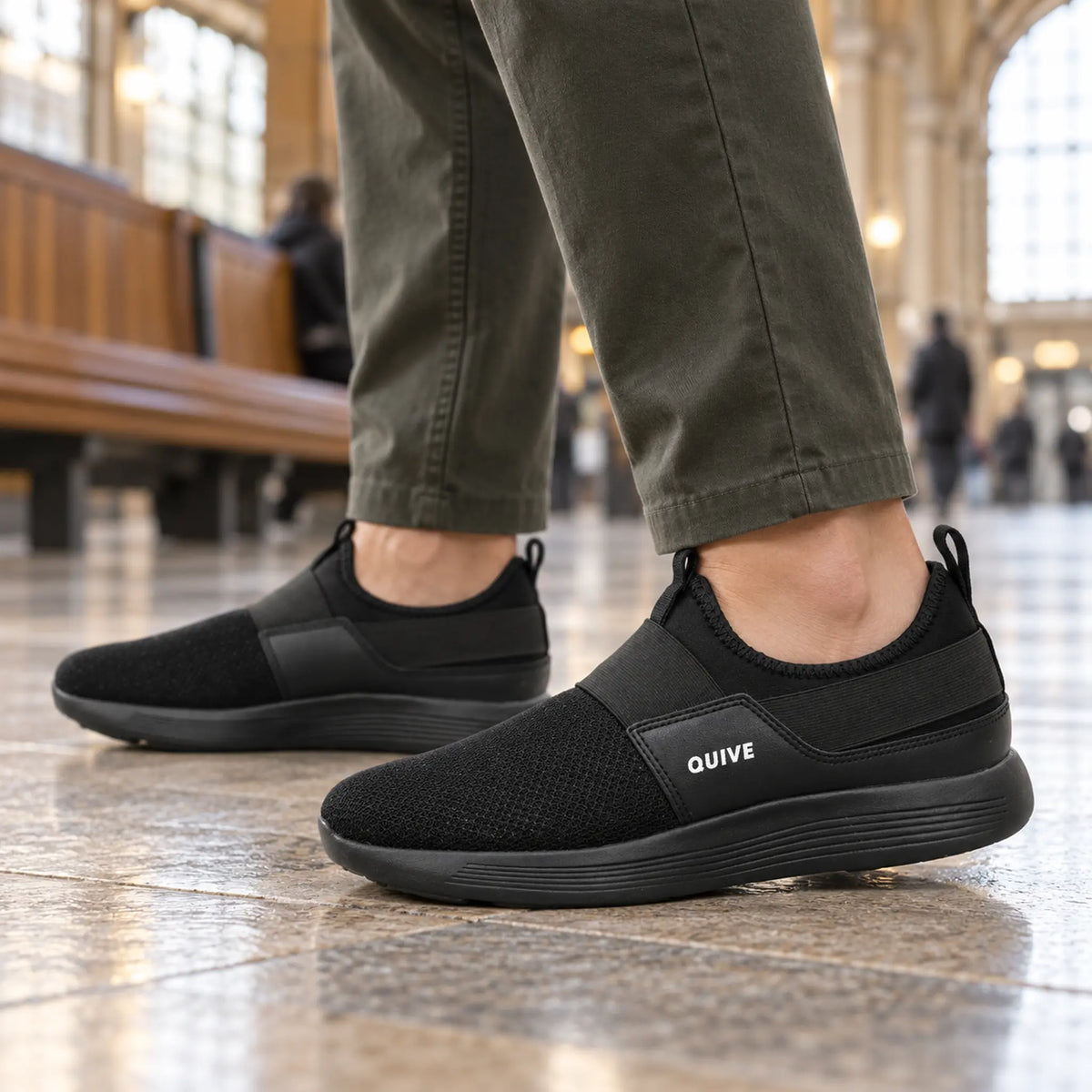 QUIVE black slip-on walking trainers worn during an urban commute