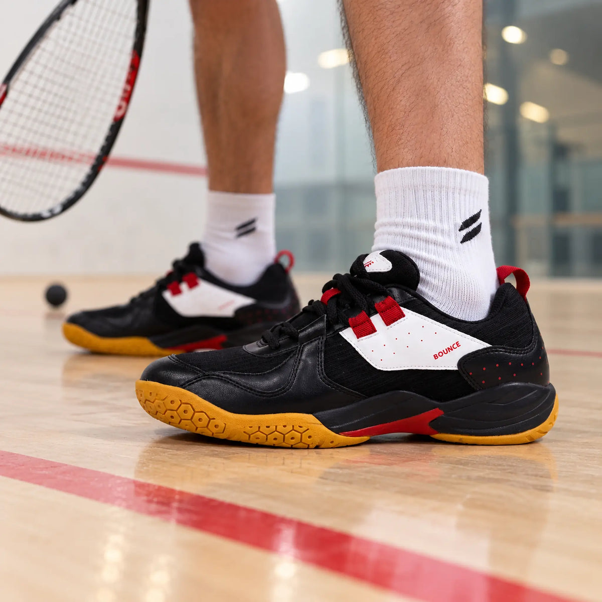 Black QUIVE Bounce court shoes worn on an indoor squash court